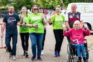 Male and females in green t-shirts smiling at the camera - one female in a wheelchair