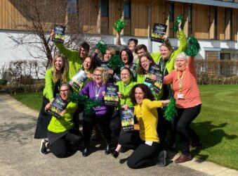 Group 1 male and females wearing mainly green holding flyers and green pom poms smiling at the camera