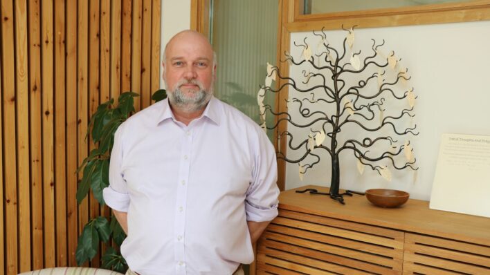 Male with a wooden wall and metal miniature tree behind