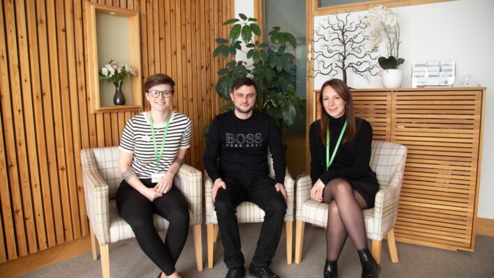 2 females and a male sitting in chairs with wooden wall behind