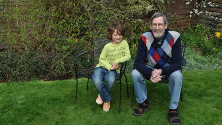 Boy and male both sitting on chairs in the garden looking at the camera