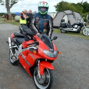 Male wearing helmet and leathers, standing next to red motorcycle