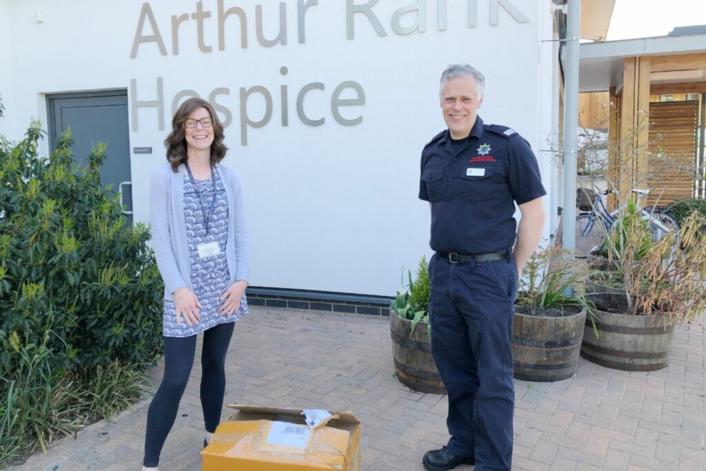 Female and male in blue uniform standing outside building with a box