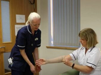 Female nurse in navy uniform with female nurse in white uniform looking at her arm
