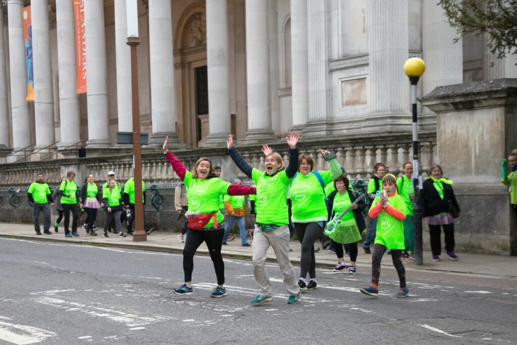 Group of adults and child walking across the road near Fitzwilliam Museum in green t-shirts