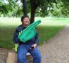 Male sitting in a green area with a large green foam finger smiling at the camera