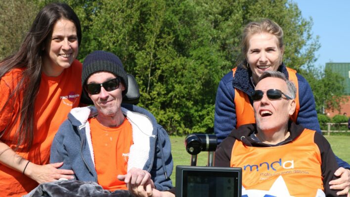2 femlaes behind 2 males wearing orange t-shirts and sitting in wheelchairs.