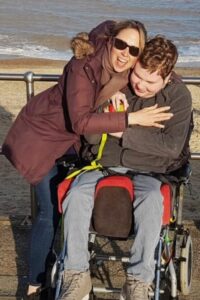 Teenage male in a wheelchair hugging female with the sea behind them