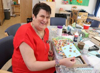 Female wearing red top sitting with crafts and smiling at the camera