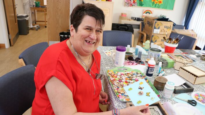 Female wearing red top sitting with crafts and smiling at the camera