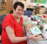Female wearing red top sitting with crafts and smiling at the camera