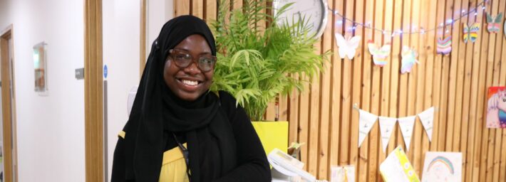 Female wearing black headress and yellow dress smiling at the camera leaning on reception desk