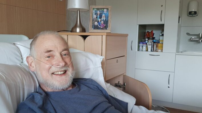 Man in bed smiling at the camera with a beard