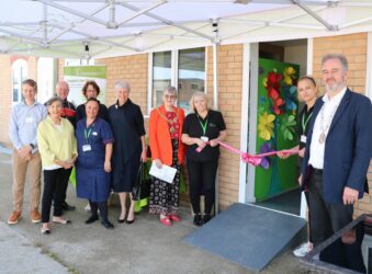 Male and females outside an open door with a pink ribbon across