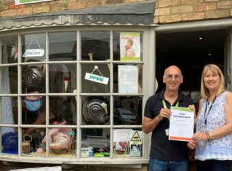 Male and female at the door of a shop holding a 5 year certificate