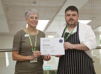 Female and male chef holding a certificate looking at the camera