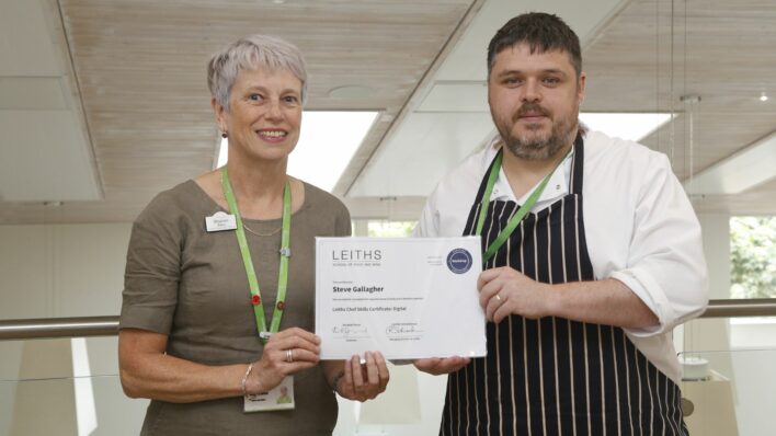 Female and male chef holding a certificate looking at the camera