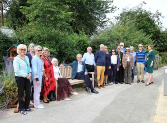 Men and women standing near a garden bench