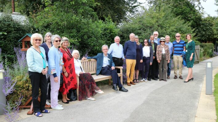 Men and women standing near a garden bench