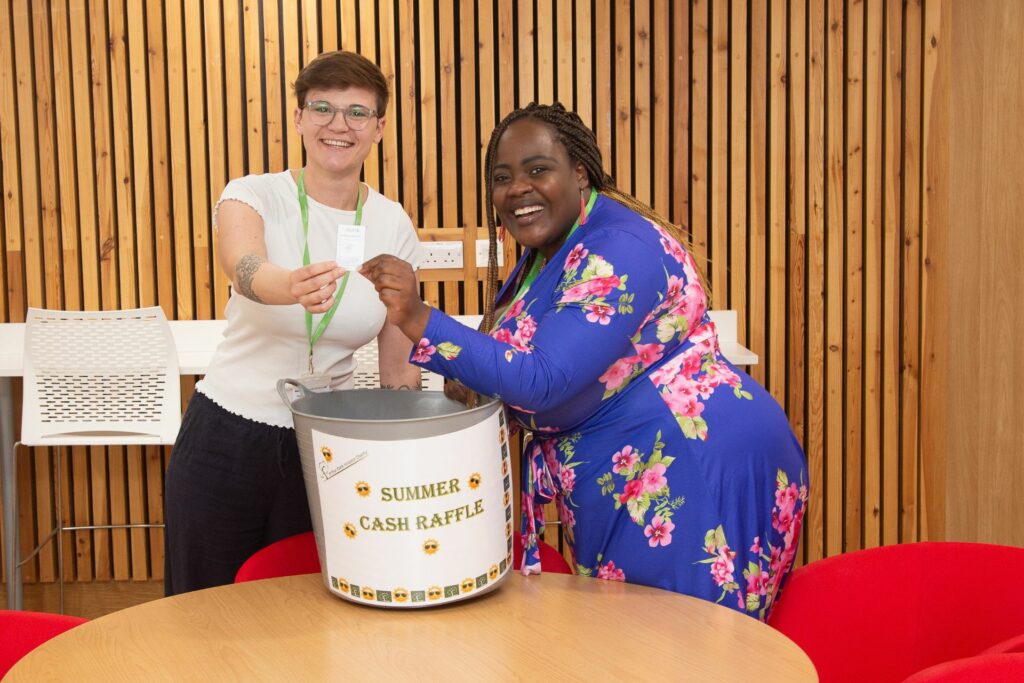 2 females holding a raffle ticket standing next to a big bucket 