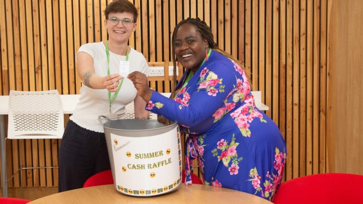 2 females holding a raffle ticket standing next to a big bucket