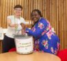 2 females holding a raffle ticket standing next to a big bucket
