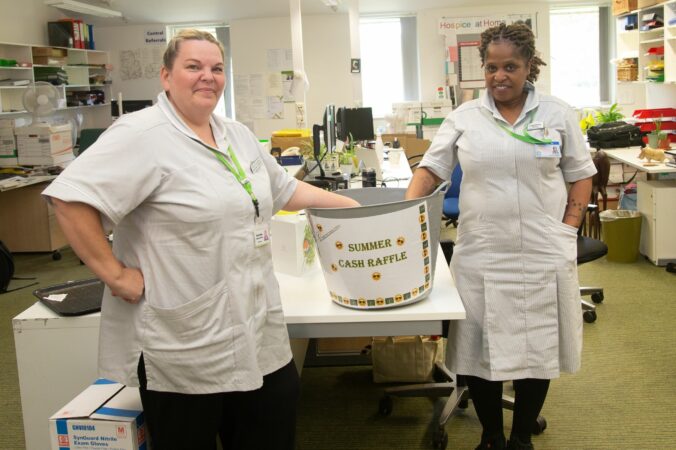 2 female nurses standing next to a big bucket of raffle tickets