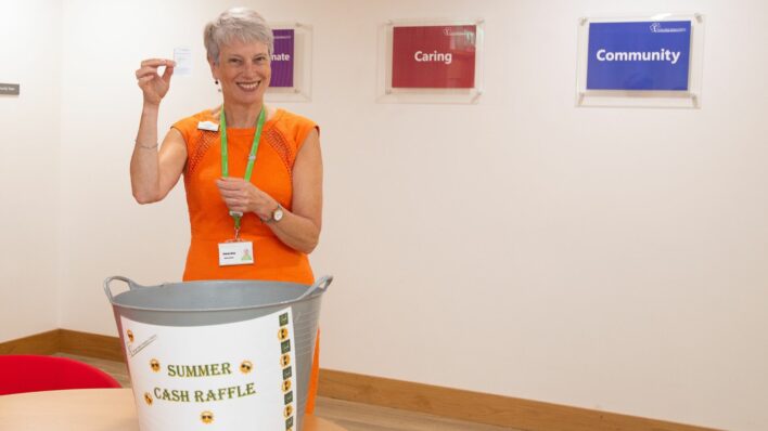 Female wearing an orange dress holding a raffle ticket up to the camera and big bucket