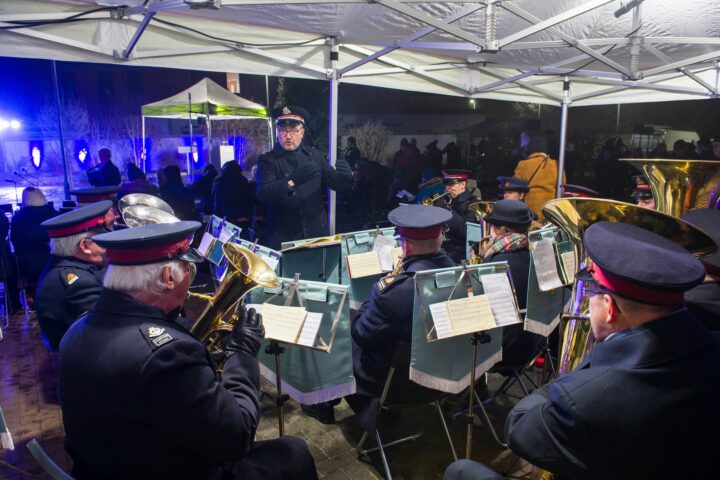 Salvation Army band conductor standing up conducting members of the band who are playing a range of brass instruments.