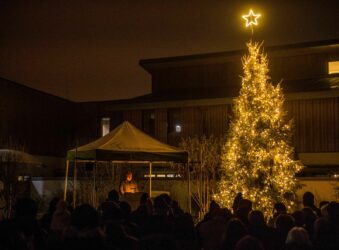 Brightly lit Christmas tree on a dark background of a group taking a moment to remember lost loved ones.