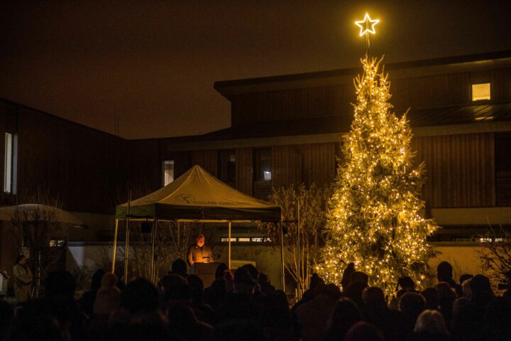 Brightly lit Christmas tree on a dark background of a group taking a moment to remember lost loved ones.