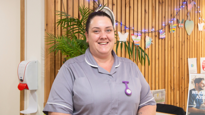 Female stood by Inpatient Unit Reception in nursing uniform.