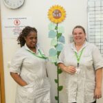 2 female nurses standing near a painted sunflower 