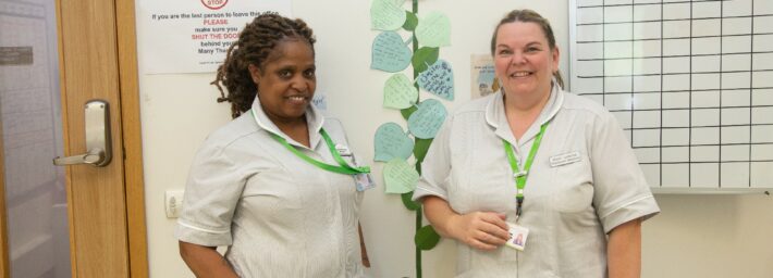 2 female nurses standing near a painted sunflower