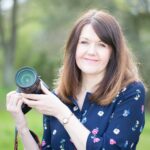Female holding a camera and looking at the camera 