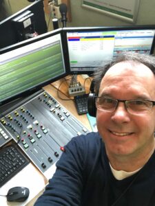 A man wearing headphones and taking a selfie in front of studio equipment