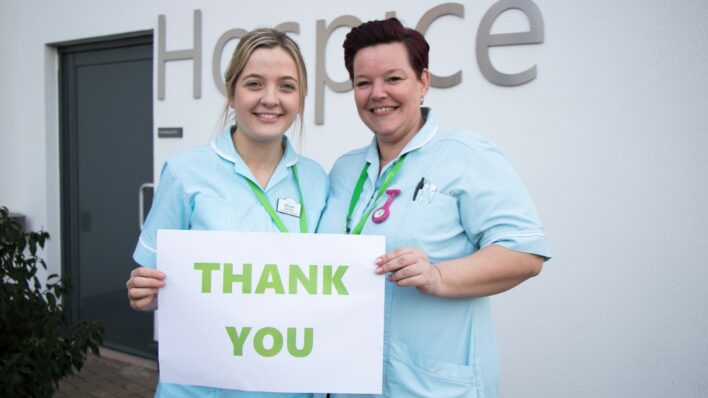 2 female nurses holding a thank you sign