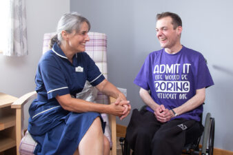 Female nurse talking to a male, sitting in a wheelchair