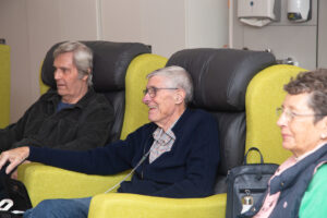 2 males and a female sitting on arm chairs - one smiling 