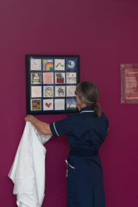 Female Nurse holding a selection of framed canvas's on a pink wall.