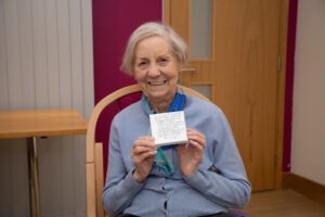 Female, holding a small canvas, smiling at the camera, sitting in a chair