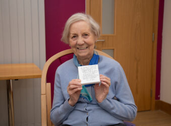 Female sitting on a chair holding a small canvas, smiling at the camera
