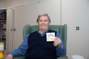 Male holding a small canvas, sitting in a chair