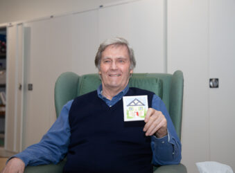 Male holding a small canvas, sitting in a chair