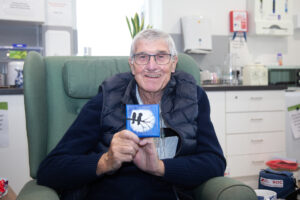 Male holding a small canvas, smiling at the camera, sitting in a chair