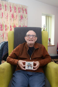 Male sitting in a chair, holding a small canvas, looking at the camera. 