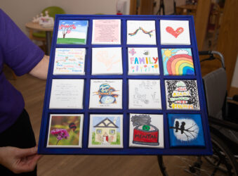 16 small canvases on a blue frame with a nurses arm holding it up