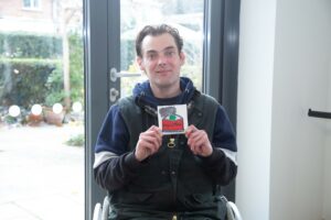 Male holding a small canvas, looking at the camera, sitting in a wheelchair