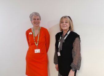 Two ladies standing next to each other and smiling at the camera