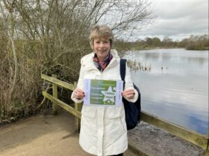 Female holding a certificate standing in front of a lake